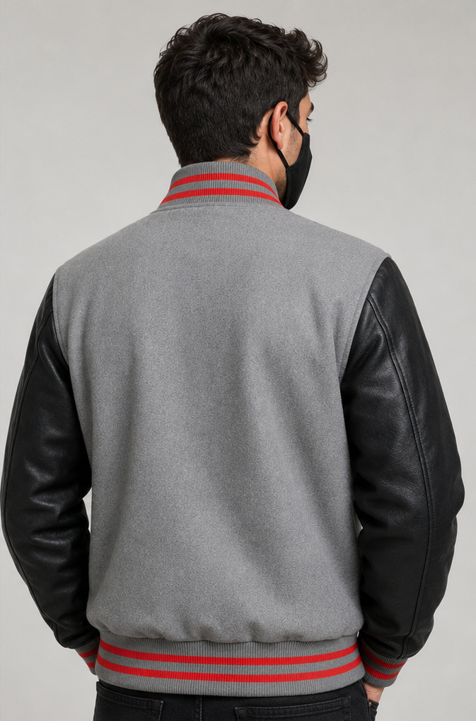 Person wearing a gray varsity jacket with black sleeves and red accents on a plain background
