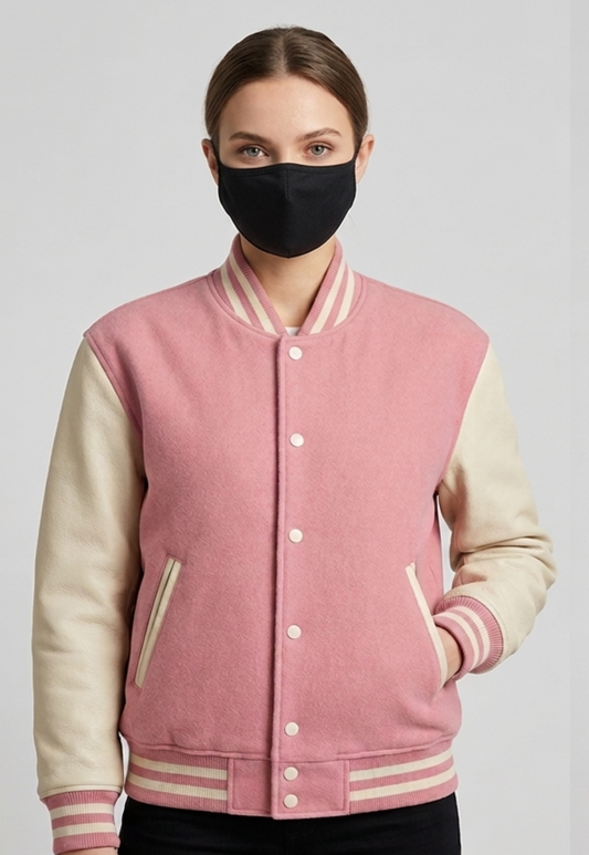 Person wearing a pink and Creamvarsity jacket with a black face mask on a gray background