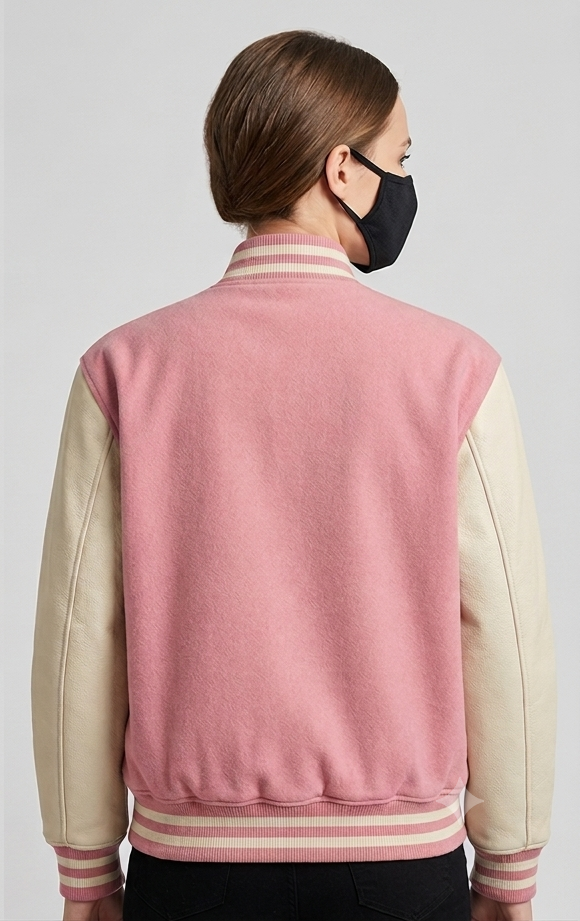 Person wearing a pink and cream varsity jacket with a black mask on a light gray background
