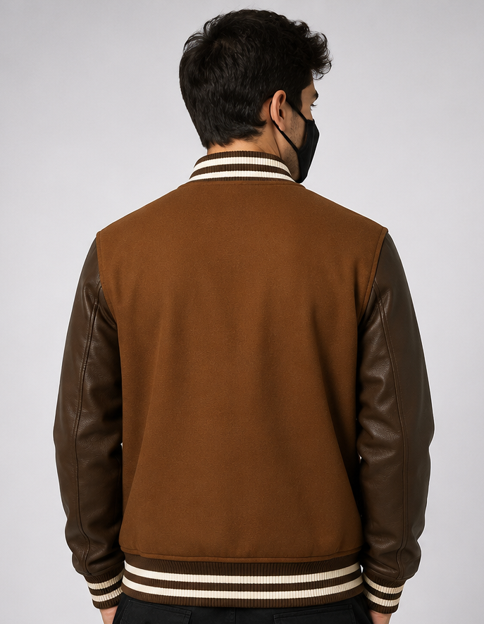 Man wearing a brown varsity jacket with leather sleeves on a plain background
