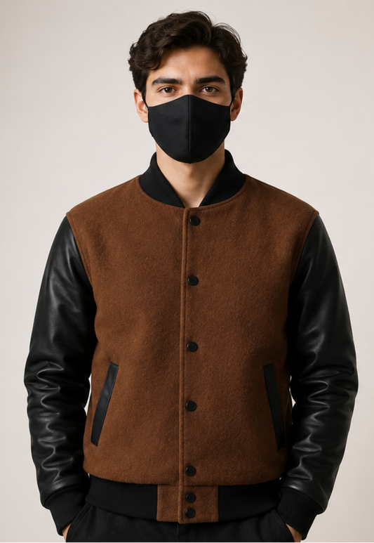 Man wearing a brown jacket with black leather sleeves and a black face mask on a plain background
