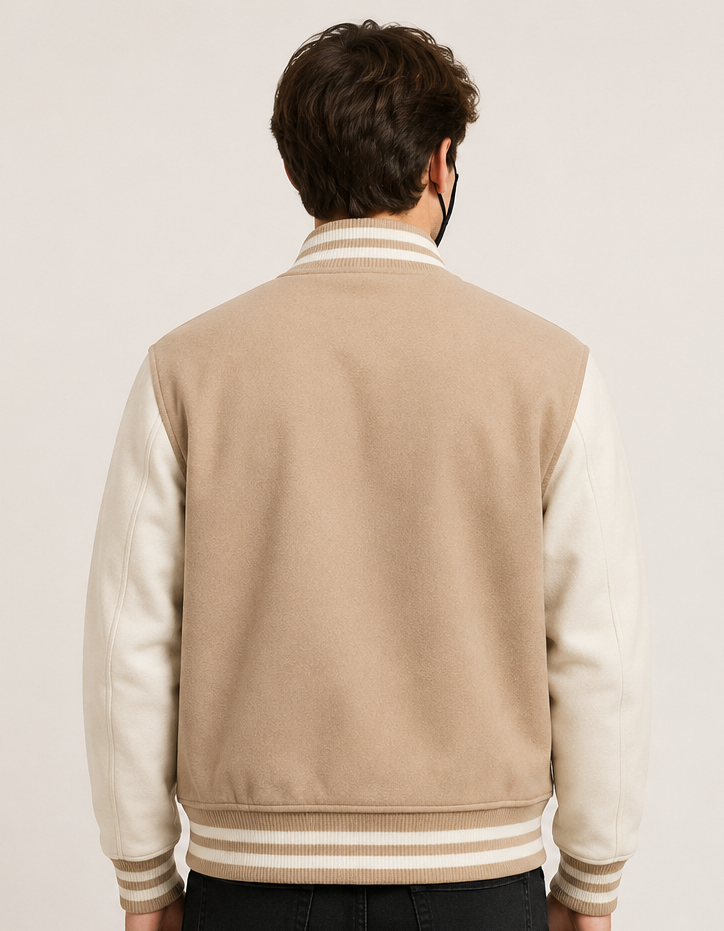 Person wearing a beige and cream varsity jacket on a plain background