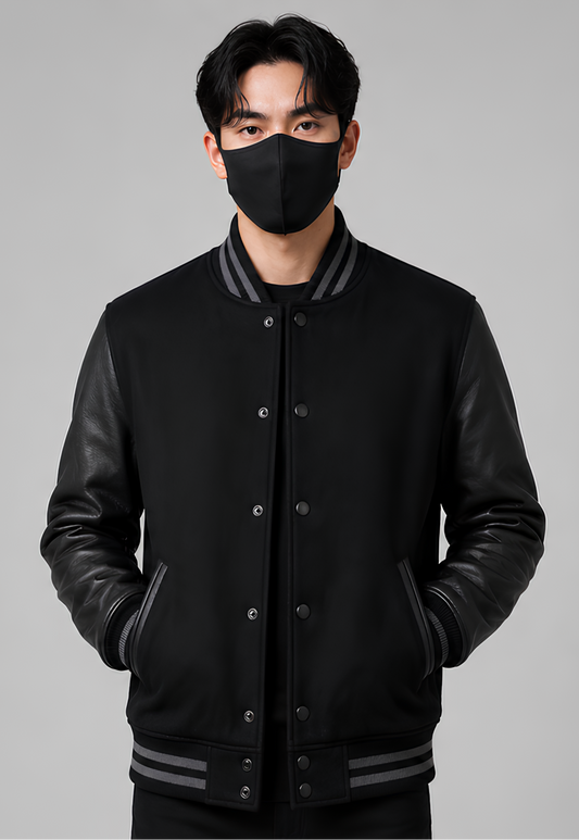 Person wearing a black varsity jacket with leather sleeves on a gray background