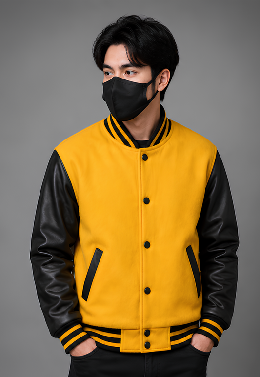 Person wearing a yellow varsity jacket with black leather sleeves on a gray background