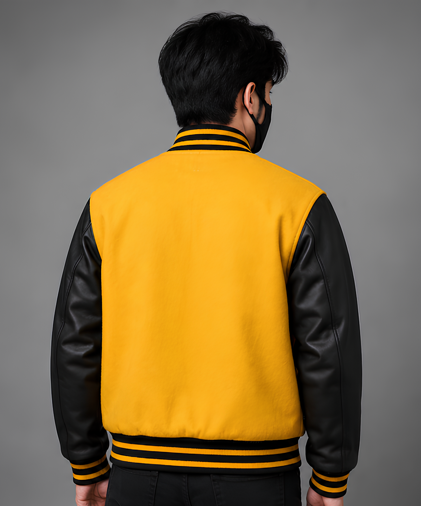 Person wearing a yellow and black varsity jacket on a gray background