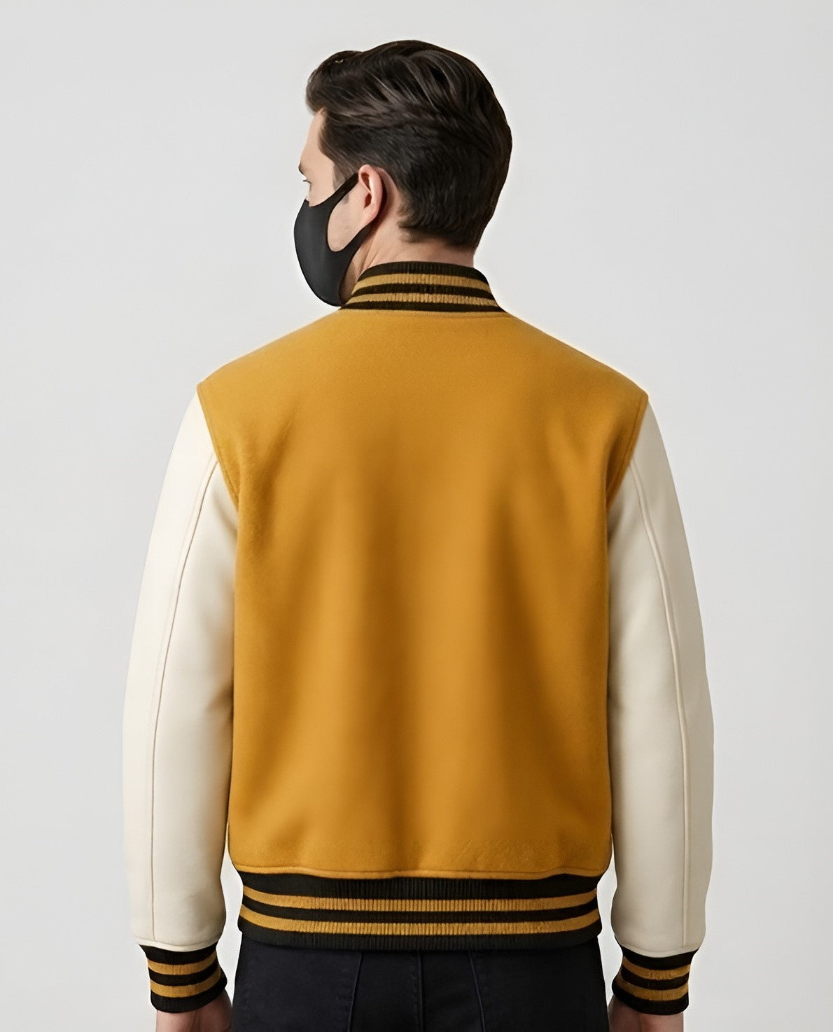 A man wearing a golden varsity jacket with white sleeves on a plain background