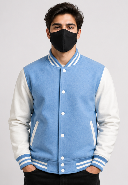 Person wearing a sky blue and white varsity jacket with a black mask on a gray background