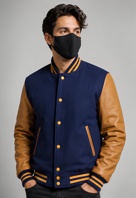 A man wearing a navy blue and Golden varsity jacket with leather sleeves on a gray background