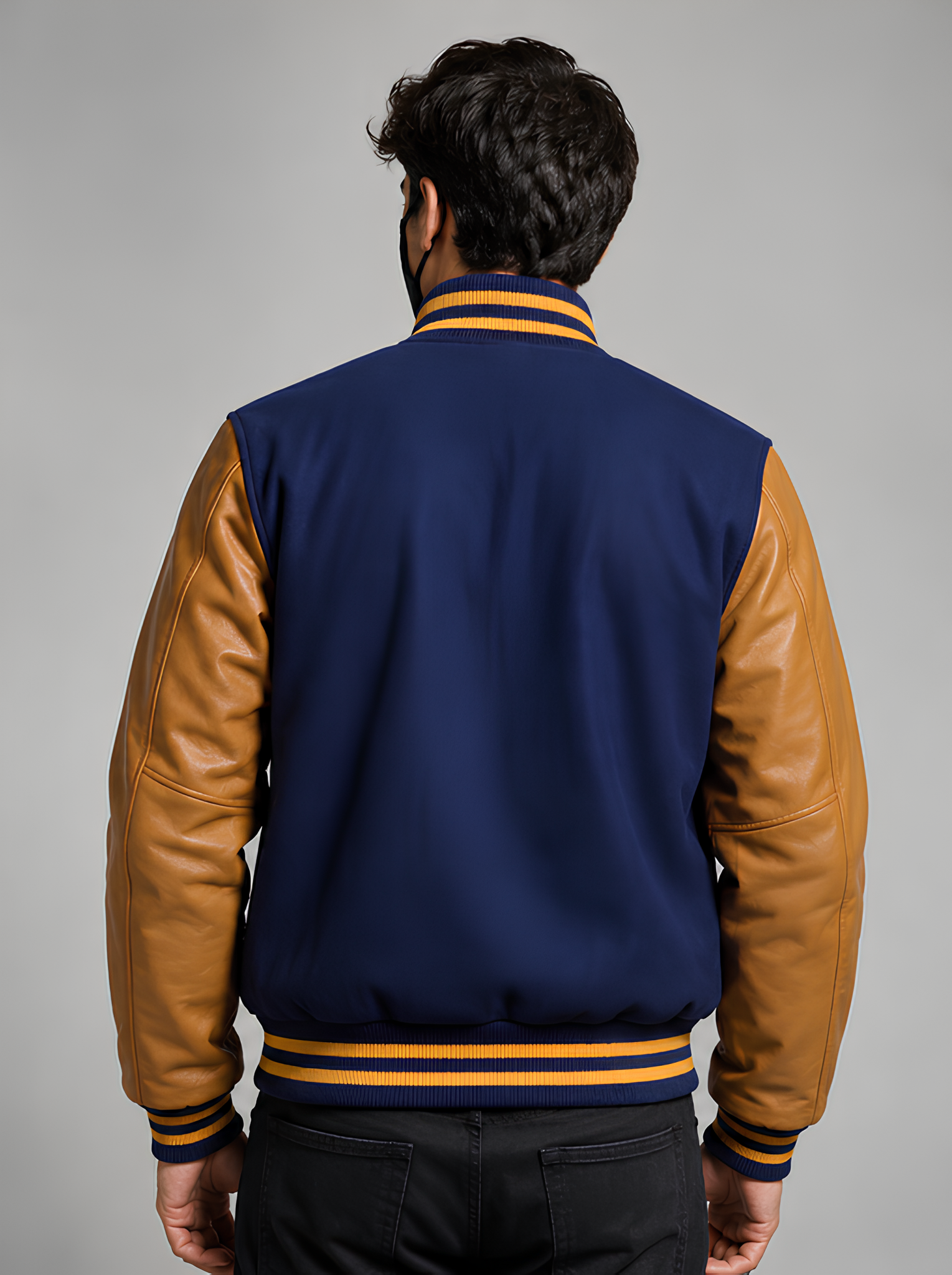 Person wearing a navy blue and Golden varsity jacket with yellow accents on a gray background