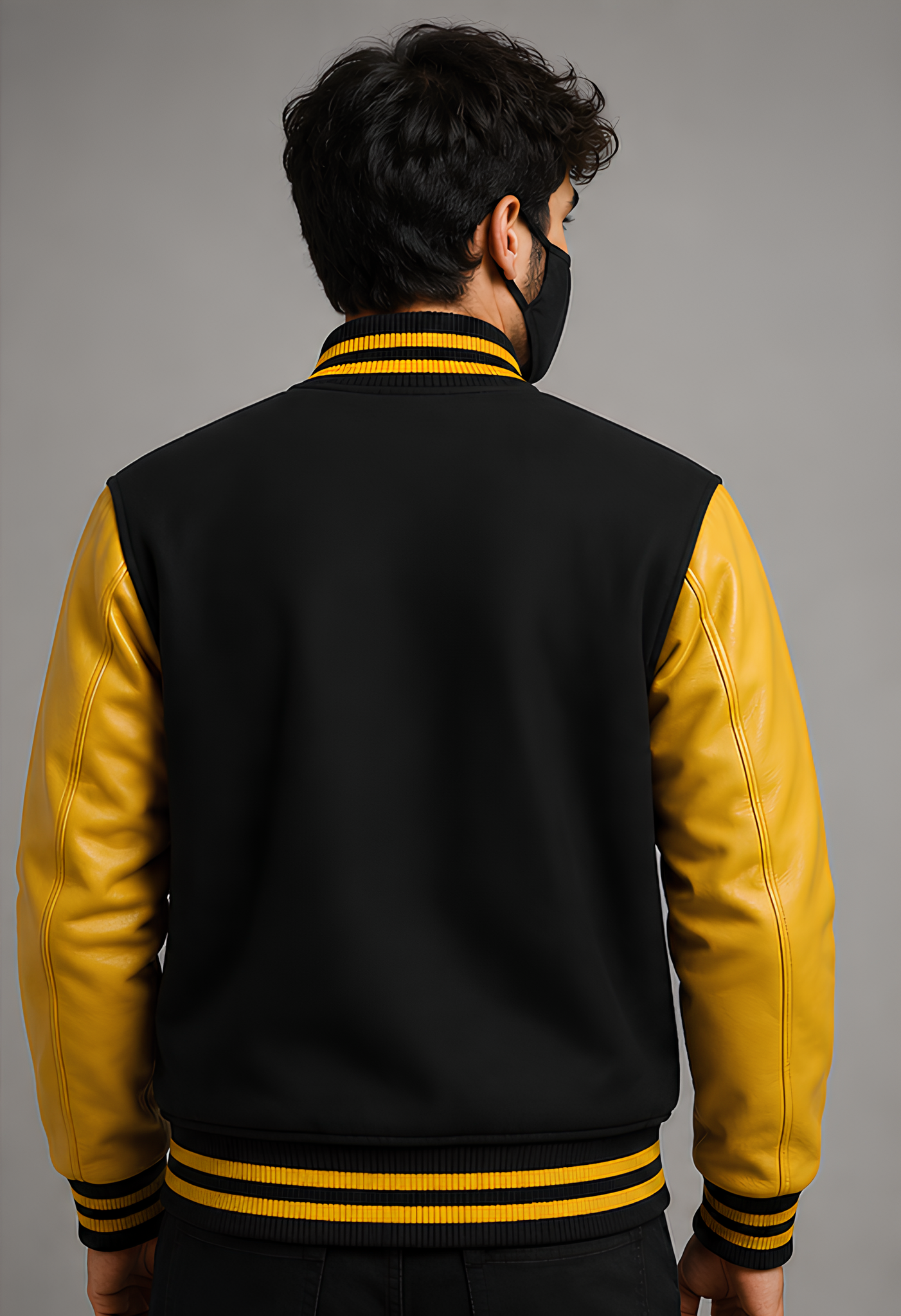 Person wearing a black and yellow varsity jacket on a gray background