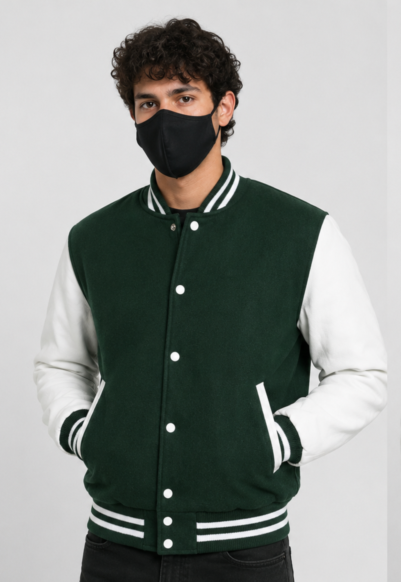 Person wearing a dark green and white varsity jacket with a black face mask on a gray background