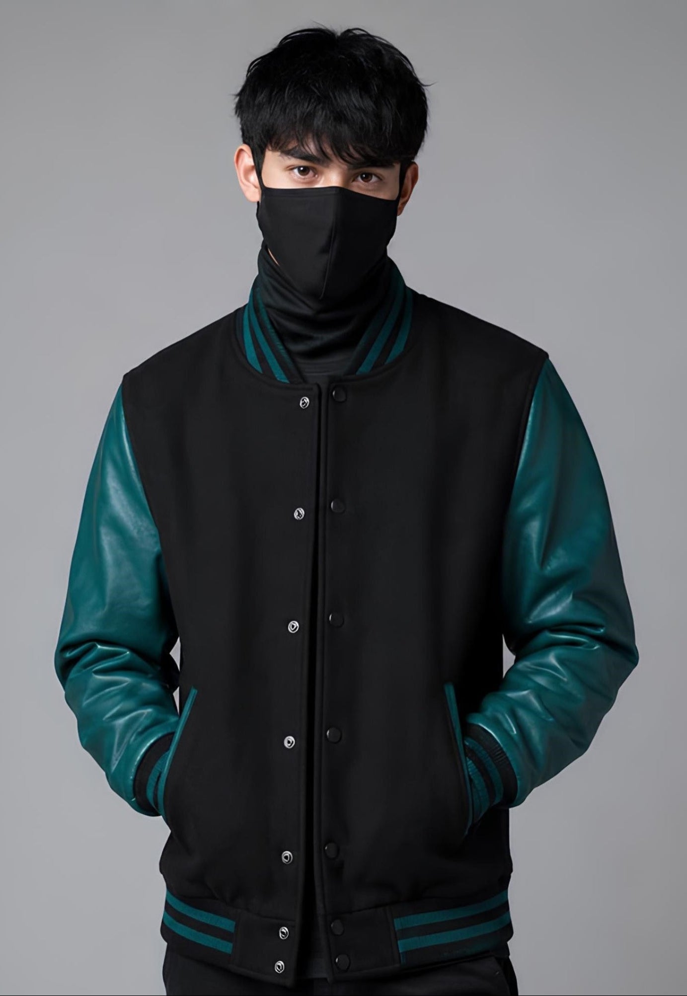 Person wearing a black and teal varsity jacket with a face mask on a gray background